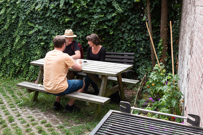 Drei Personen sitzen an einem Tisch im grünen Garten.