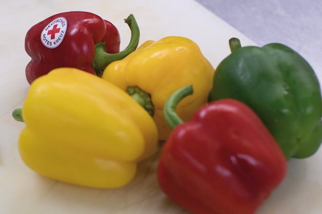 Fünf bunte Paprika, eine mit Rotkreuz-Aufkleber.