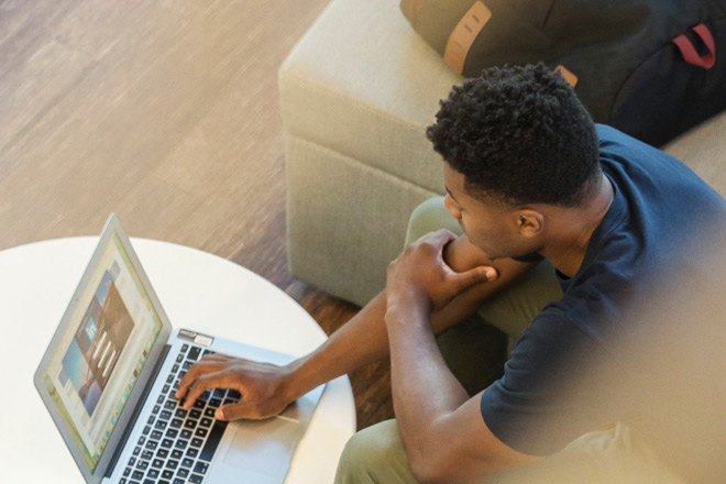 Ein männlicher Teenager mit Migrationshintergrund arbeitet an einem Laptop.
