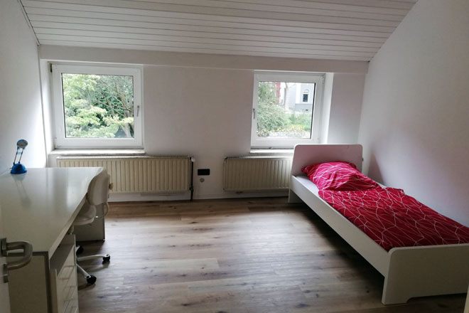 Ein Zimmer in der Einrichtung Kempen II mit Bett, Tisch und zwei Fenstern.