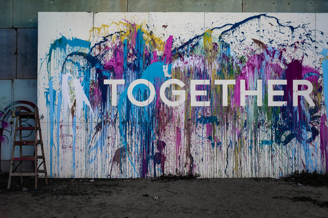 Schriftzug "Together" auf einer Wand mit bunten Farbspritzern.