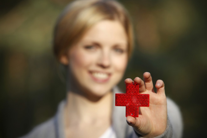 Junge blonde Frau hält einen Reflektor in Form eines roten Kreuzes in die Kamera.