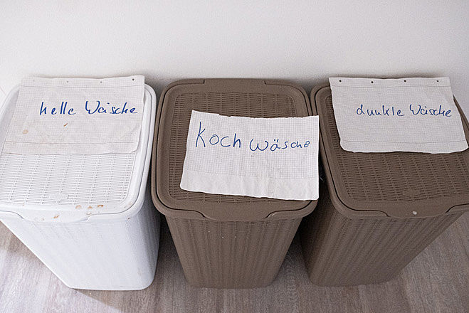 Drei Wäschekörbe, beschriftet mit "helle Wäsche", "Kochwäsche" und "dunkle Wäsche".