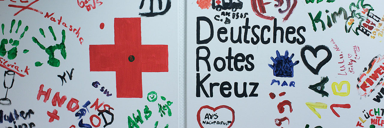 Buntes Wandbild aus Fingerfarben mit dem Logo des Deutschen Roten Kreuzes.