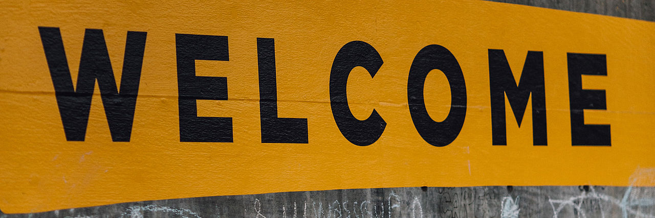 Schwarzer Schriftzug "Welcome" auf gelbem Grund.
