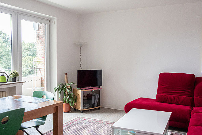 Wohnzimmer mit roter Couch, Fernseher und Esstisch.