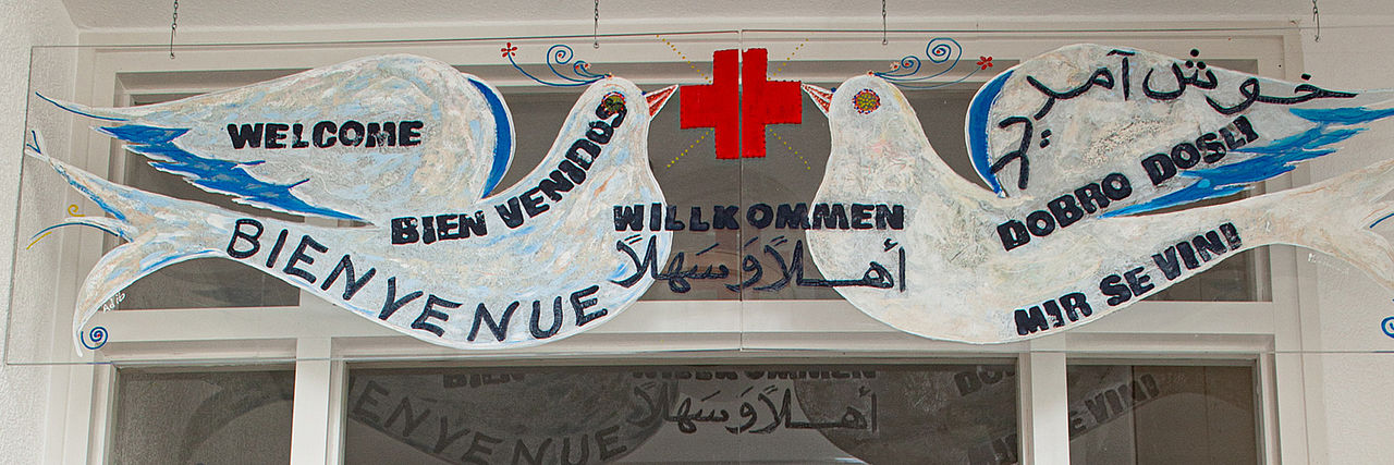 Zwei gemalte Tauben mit rotem Kreuz und dem mehrsprachigen Schriftzug "Willkommen".