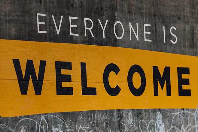 Schriftzug "Everyone is welcome" in weißen und schwarzen Buchstaben auf gelbem und grauem Grund.